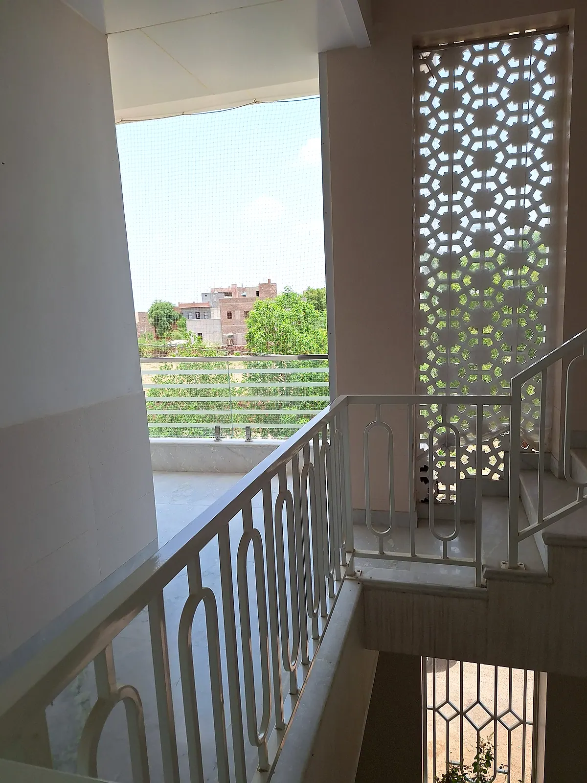 Bright stair landing with railing, protective mesh, decorative ventilation screen and neighbourhood greenery
